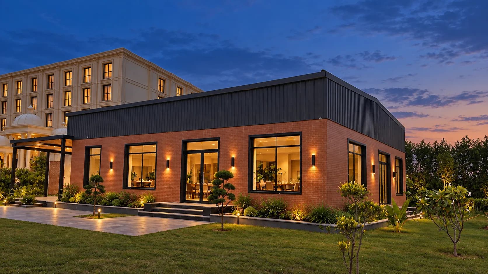 The restaurant at dusk: a single-storey brick building with tall lit windows, the hotel beyond and a deep blue sky