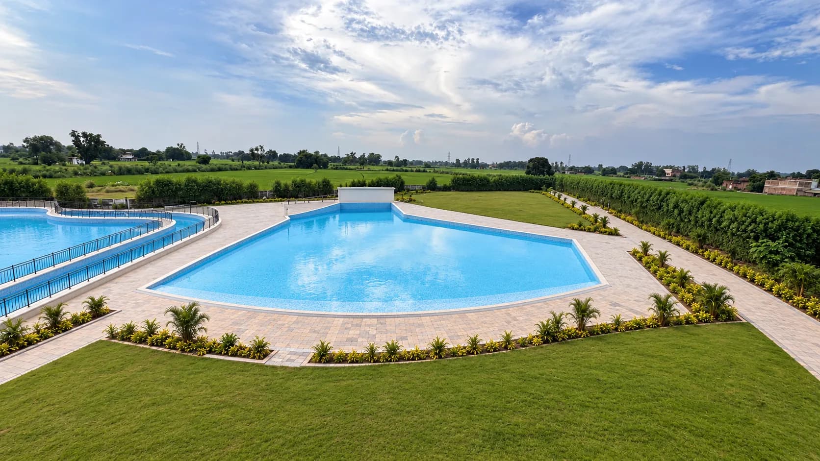 The wave pool on a bright day: a wide sweep of blue water, a pale stone deck and lawn, fields beyond